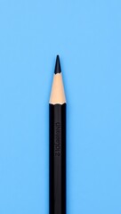 Vertical black pencil with sharp tip on textured blue background. Wood grain contrasts smooth casing. Lighting and focus highlight precision, simplicity, and clean design.

