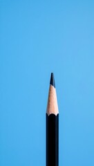 Vertical black pencil with sharp tip on textured blue background. Wood grain contrasts smooth casing. Lighting and focus highlight precision, simplicity, and clean design.

