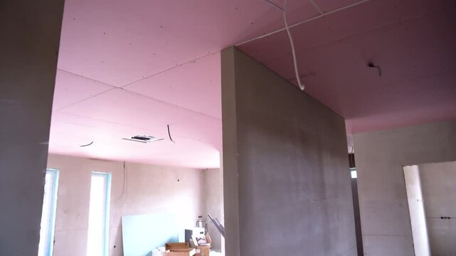 Interior view of unfinished drywall construction with exposed pink ceiling panels and wiring