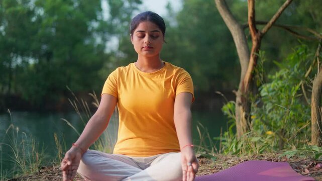 Tranquility woman sitting in easy position meditating with gyana mudra by a serene lake in the morning sunlight.