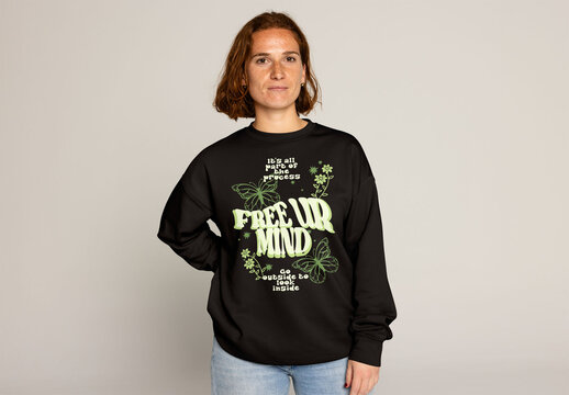 Jumper mockup. A young woman, with short hair and jeans, is posing in a plain sweatshirt against a neutral background and looking at camera.