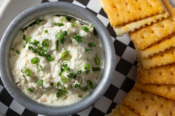 A top down view of a condiment cup of pimento cheese dip, with saltine crackers.