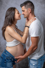 A man is about to kiss his pregnant partner while holding her belly with his hands