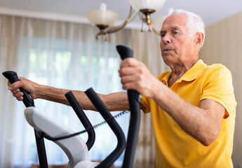 Senior man training on cross-trainer at home