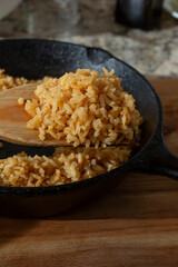 A view of a wood spatula scooping Mexican rice in a cast iron skillet.