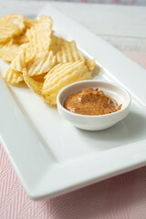 A view of a pile of pepper flavored ridged potato chips, with chipotle dip, on a platter.
