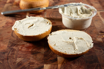 A view of a butter knife spreading some dairy-free cream cheese, on a gluten-free bagel slice.