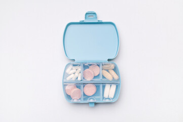 Blue pill organizer, pillbox with different vitamins, capsules, tablets, pills, dietary supplements on gray background flat lay top view. Medical pharmaceutical concept, health and beauty