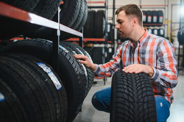 male studying car tire in market, guy in casual wear stand looking at tire, make choice. shopping...