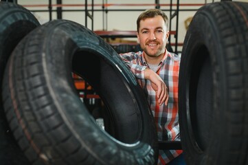 Smart male customer choosing new tires in the supermarket for buying. Big shopping mall with car...