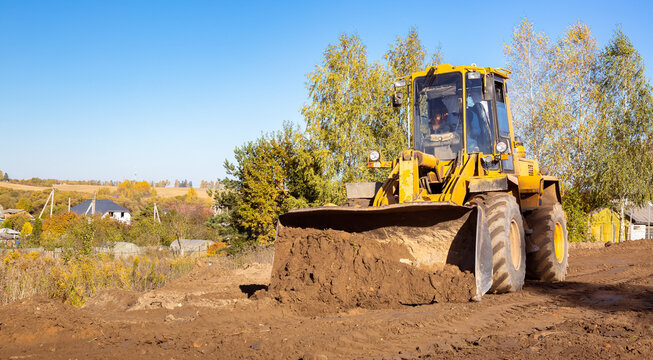 Yellow bulldozer at a construction site. Big wheel excavator leveling and clearing the land plot side view. Moving earthworks soil. Copy space. Building area. Special transport. High quality photo.