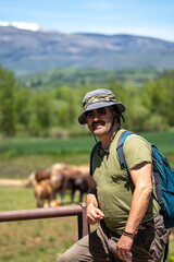 Caucasian hiker with backpack and hat enjoying mountain scenery looking at camera