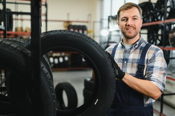 Car tire service concept. Portrait man mechanic holding new tyre on background store