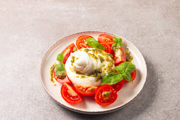 Burrata cheese caprese salad with cherry tomatoes, olive oil, pesto and seasoning. Fresh food concept. 