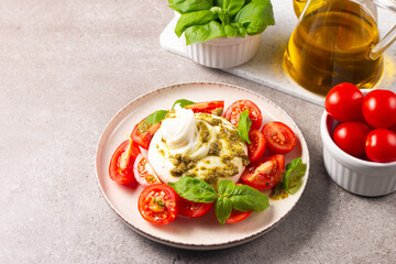 Burrata cheese caprese salad with cherry tomatoes, olive oil, pesto and seasoning. Fresh food concept. 