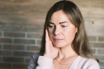 Woman with hand on face, looking down, conveying sadness, contemplation, or stress indoors against...