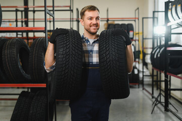 Portrait of smiling warehouse worker standing by the pile of new car tires