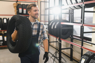 Hardworking experienced worker holding tire and he wants to change it In the tire store. Selective...