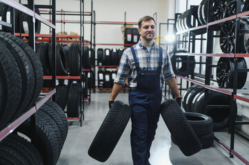 Portrait man mechanic holding new tyre on background store, car tire service concept