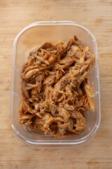 A view of a food plastic container of crockpot BBQ chicken on a plate.