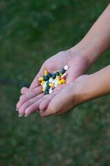Dłoń dorosłej osoby trzymająca różnokolorowe tabletki i kapsułki. Zbliżenie na leki w dłoni. Koncepcja farmacji, uzależnienia od leków, suplementacji i medycyny.
