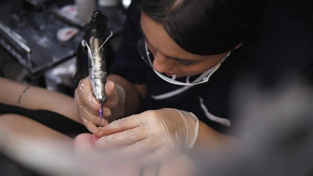 A close-up shot of a female professional tattooing a client's lips in a beauty salon, using permanent lip makeup, a modern technique in cosmetology.
