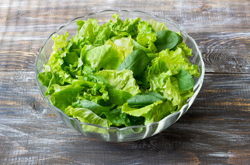 Fresh green lettuce and spinach salad in glass bowl on rustic wooden table, healthy organic food