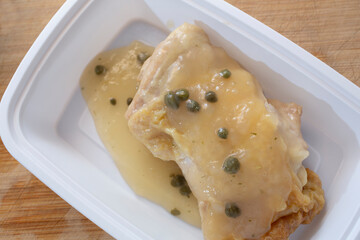 A top down view of a white container of chicken piccata.