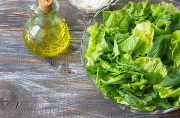 Fresh green salad leaves with olive oil and pickled onion, top view on rustic wooden background