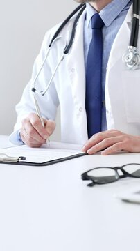 Male doctor writing a prescription and filling out medical records on a clipboard in an office setting, showcasing the essential aspects of healthcare and patient care. Medicine and health care
