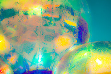 A vibrant, abstract artwork featuring a close-up of a shiny, surface reflecting multicolored light. The dominant hues are red, orange, yellow, and pink, with hints of blue and green.