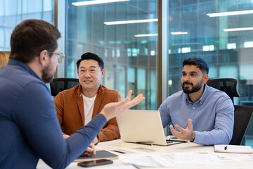 A diverse business team meeting in a modern office setting. Three colleagues collaborate around a...