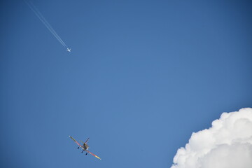 An aerobatic aircraft flying low with a high-altitude jet airliner in the background, captured on a...