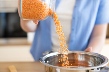 A hand pours vibrant red lentils into a shiny steel bowl, showcasing the beauty of cooking and...