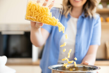 A joyful moment captured of a person pouring pasta into a pot while cooking in a cozy kitchen...