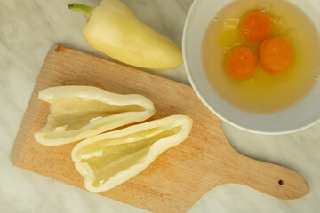 halved peppers cracked eggs in bowl on cutting board
