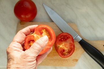 hand holding halved tomato on cutting board 