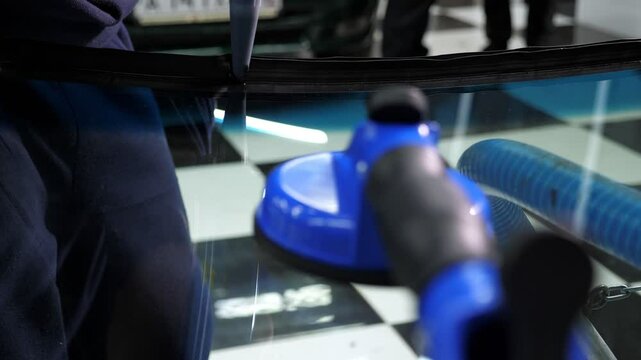 A close-up of the windshield repair process in a car service, blue professional suction cups are visible on the glass. The master applies glue.
