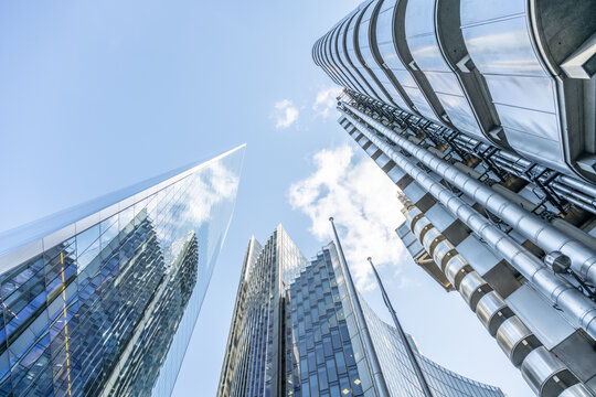 Towering skyscrapers dominate the skyline of London's financial district, showcasing sleek glass facades that reflect the clear blue sky. The urban landscape embodies modern architecture.
