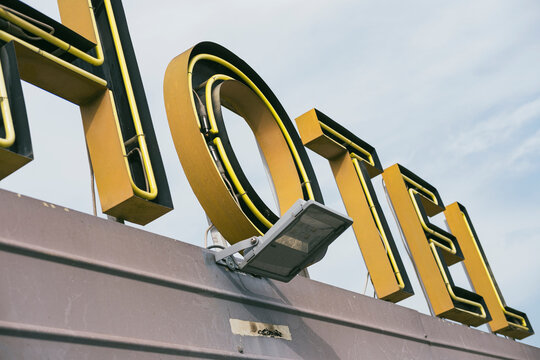 Vintage hotel sign with yellow letters against overcast sky, capturing urban travel iconography, roadside accommodation, and nostalgic aesthetics in modern travel photography context