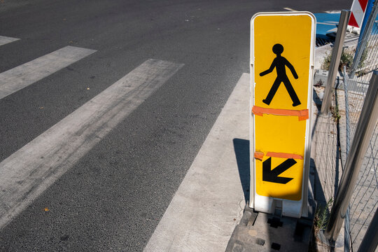 Urban pedestrian crossing sign on yellow background with arrow pointing sideways, highlighting city travel routes, urban navigation, and public infrastructure essential for modern travel