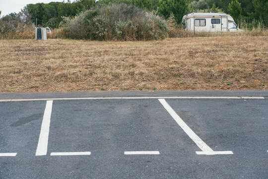 Empty asphalt parking lot in rural landscape with caravan visible in background, symbolizing road travel, temporary stops, and minimalist infrastructure along modern travel routes