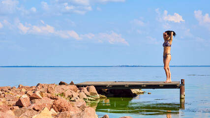 Young pretty woman in swimsuit standing on pier on shore