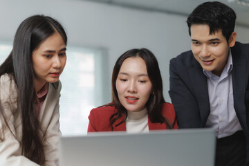 Three colleagues gather around a laptop, actively discussing and collaborating on a business...