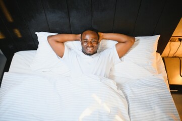 portrait of relaxed smiling African American man lying on white bedsheets at home