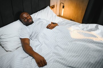 portrait of relaxed smiling African American man lying on white bedsheets at home