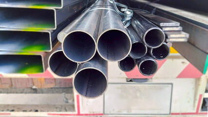 Black steel pipes neatly stacked in an industrial warehouse, used in construction, plumbing, and structural applications.