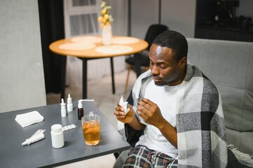 rhinitis, medicine and healthcare concept sick african american man in blanket using nasal spray at...