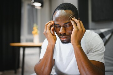 Closeup of young african american man suffering from headache at home, touching his temples....