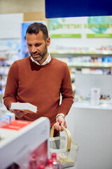 Man Shopping for Products in Pharmacy Holding Basket and Reading Labels